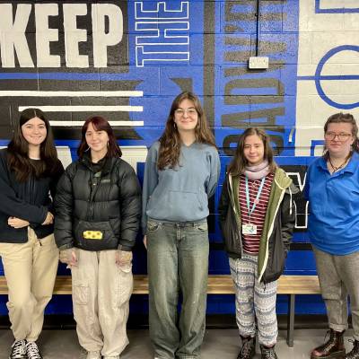 Coleg Menai art students in front of the mural they painted in the home dressing room at Nantporth Stadium