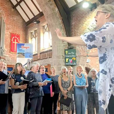 Sara Brown yn arwain côr Coastal Voices a Chôr Cymunedol Bangor yn Eglwys Ddiwygiedig Unedig Llandrillo-yn-Rhos