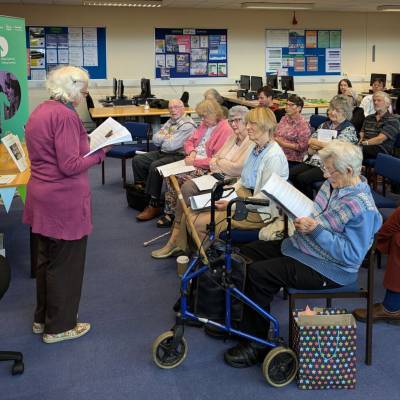 Dysgwraig yn darllen ei gwaith yn ystod lansiad y llyfryn ysgrifennu creadigol yn y llyfrgell ar gampws Coleg Menai ym Mangor