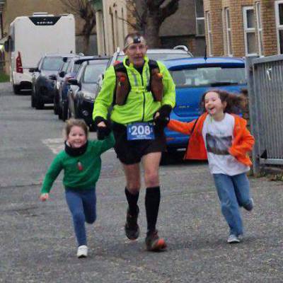 Tecwyn Jones running to the finish line of the Pen Llŷn Winter Ultra with granddaughters Tesni and Casi