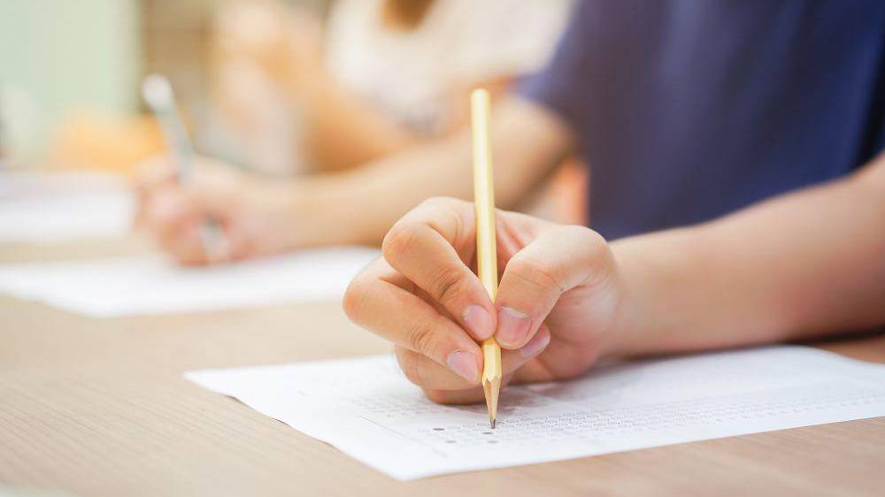 Closeup student hand using pencil for doing text exam