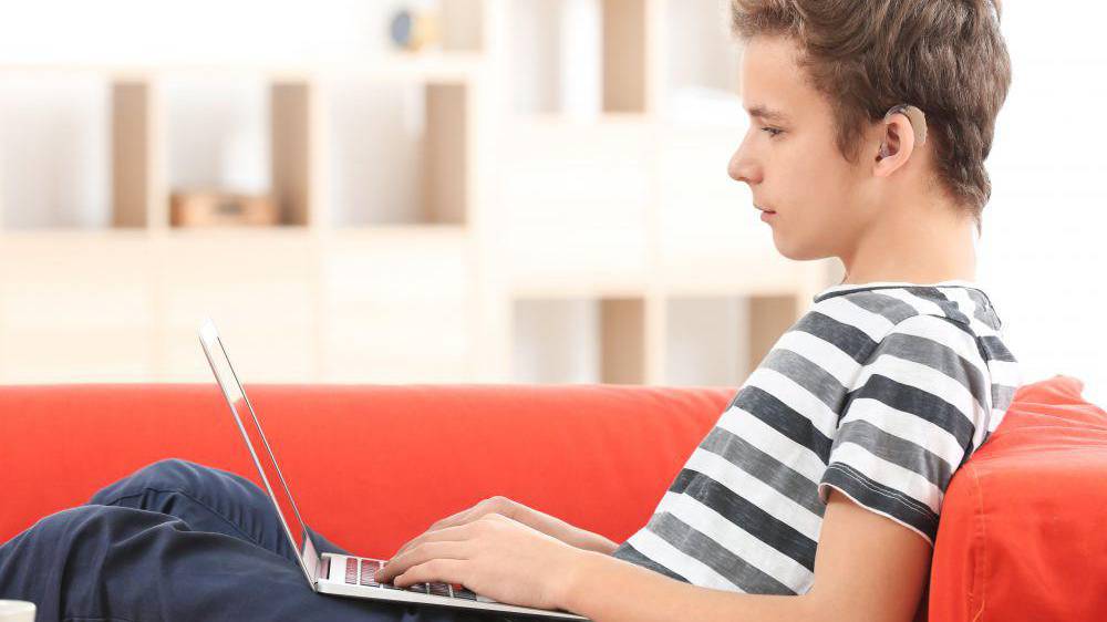 Teenage boy with hearing aid using laptop indoors